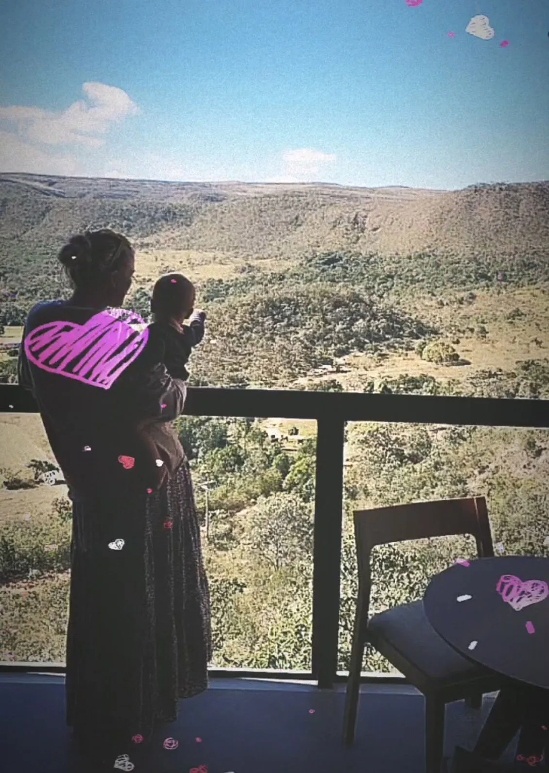 A silhouette of Antonio's wife holding a child looking out at a mountainous landscape, with artistic hearts overlay